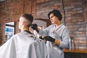 Peluquería hermosa mujer afeita la cabeza del cliente con una recortadora eléctrica en peluquería. concepto de publicidad y peluquería. foto