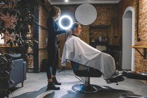 Mujer peluquería afeita la cabeza de un cliente sentado en una silla con una recortadora eléctrica en una peluquería foto