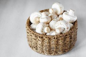 Champiñones champiñones en una canasta de mimbre redonda sobre una mesa de madera blanca foto