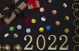 New Year 2022. Top view New Year mockup on black shiny background red ribbon, gift box, gold numbers and multicolored sparkles. Layout of postcards,