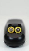 Black remote control with yellow AAA batteries on a white background. Battery replacement, spare parts. Remote control battery compartment close-up. Vertical photography photo