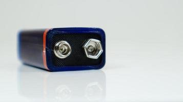 una batería pp3 azul usada sobre un fondo blanco con reflejo. batería principal para fuentes de alimentación personales. primer plano de un conector de batería rayado y usado. foto