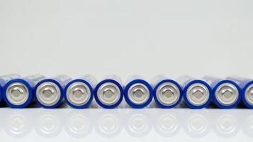 Lots of AA alkaline batteries on a white glossy background with reflection with copy space lined up in one line.
