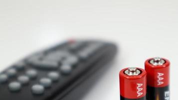Black TV remote control with AAA alkaline batteries in red and white on a white background. Battery replacement, spare parts. Remote control battery compartment close-up. photo