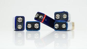 cinco baterías pp3 azules usadas, dispuestas caóticamente y dispersas sobre un fondo blanco con reflejo. batería principal para fuentes de alimentación personales. primer plano de un conector de batería rayado y usado. foto