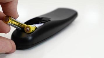 Insert the AAA size battery into the remote control. Installing batteries in the wireless device. A male hand holds a yellow alkaline battery. Text in English and Russian. photo