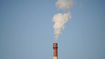 A tall chimney with white smoke on a blue sky background video