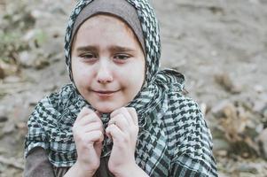 un niño refugiado en la guerra, una niña musulmana con la cara sucia en las ruinas, el concepto de paz y guerra, el niño llora y espera ayuda. foto