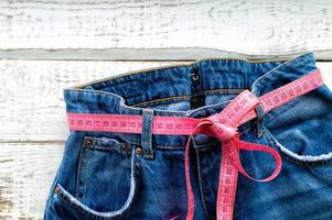 Top of denim trousers, on a wooden background. Blue jeans with a measuring tape instead of a belt. jeans with a measuring tape around the waist. The concept of a healthy lifestyle and diet. photo