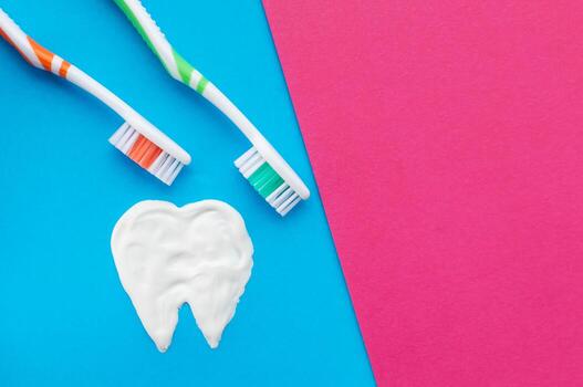 Cepillos de dientes multicolores sobre un fondo azul y rosa con un patrón de dientes dibujado con pasta de dientes. la vista desde la cima. foto