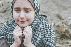 un niño refugiado en la guerra, una niña musulmana con la cara sucia en las ruinas, el concepto de paz y guerra, el niño llora y espera ayuda. foto