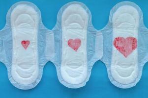 Women's pads with red hearts of different sizes on a blue background. The concept of the menstrual cycle. photo