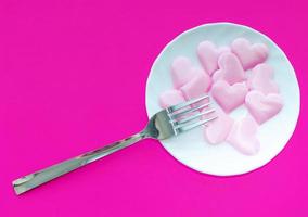 Pink hearts and a fork on a white plate on a pink background with space for writing. The view from the top. photo