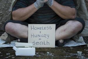 un vagabundo se sienta en la calle con un cartel y una caja de donaciones. pobreza, hambre, desempleo. foto