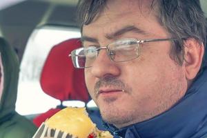 man wearing spectacles eats sandwich photo