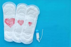 Women's pads with red hearts of different sizes and a tampon on a blue background. The concept of the menstrual cycle. photo