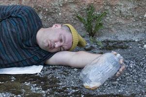 un vagabundo que está ebrio duerme en la calle con una botella de cerveza en la mano. pobreza, desempleo, alcoholismo. foto