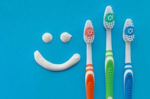 Cepillos de dientes multicolores sobre un fondo azul con una sonrisa pintada con pasta de dientes. la vista desde la cima. foto