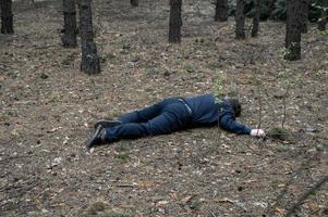 Murder in the woods. The body of a man in a blue shirt and trousers lies on the ground among the trees in the forest. Victim of an attack. photo