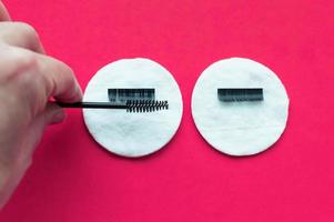 the hand of the eyelash extension master combs artificial eyelashes with a brush on a cotton swab on a pink background. photo