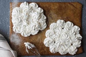 Delicate white meringue cakes for Pavlov's dessert are placed on a wooden Board next to a linen napkin. Build process. photo