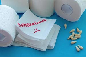 Toilet paper with the word hemorrhoids next to toilet paper rolls and anal candles on a blue background. photo