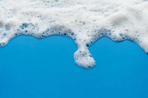 The soapy foam texture flows down from the top on a blue background. The concept of hygiene. photo