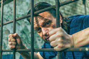 un hombre deprimido esposado tras las rejas. encarcelan a un delincuente varón deprimido y arrestado. grita, rompe, llora. foto