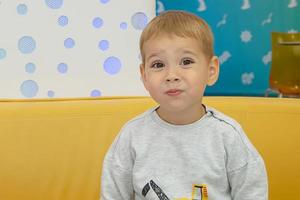 Un niño hermoso y alegre hace muecas en un café en una mesa en el patio de comidas del centro comercial. compras. foto