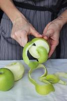 Hands of the cook peel a green Apple with a knife. Homemade cake. Housework. photo