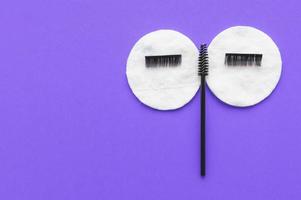 The concept of eyelash extension. Face made of brushes, cotton pads and artificial eyelashes on a lilac background with a place for writing. photo