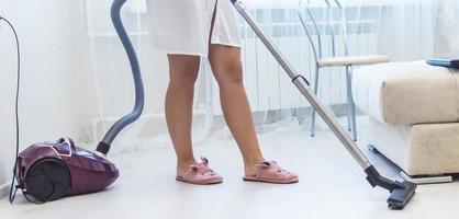 a girl in slippers and a bathrobe vacuuming the floor in an apartment. selective focus. film grain. photo