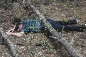 A body in the woods. A dead man in a blue t-shirt and trousers is pinned down by a fallen tree. Concept of accidents in the forest.