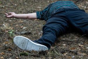 Murder in the woods. The body of a man in a blue t-shirt and trousers lies on the ground among the trees in the forest. Victim of an attack. photo