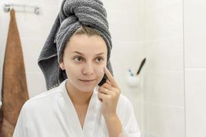 la niña en el baño frente al espejo con una toalla en la cabeza se aplica crema en la cara. enfoque selectivo. grano de la película