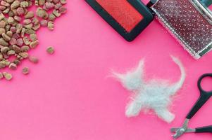 Comb, food and scissors after cutting the cat and a piece of cat hair in the shape of a cat on a pink background. The view from the top. photo
