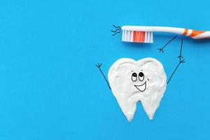 Cepillo de dientes naranja en forma de personaje de dibujos animados sobre un fondo azul con un patrón de dientes dibujado con pasta de dientes juntando sus manos.El concepto de salud dental. foto