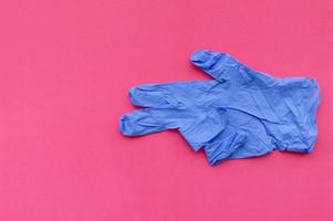 A blue medical glove on a pink background points with two fingers at an empty space for text. Selective focus. photo