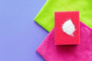 Cleaning powder on a red sponge for washing dishes on a household towel on a lilac background. The concept of homework.