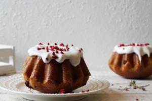 Rum baba poured with white icing on a plate on a table covered with a white tablecloth.