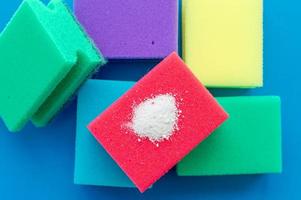 Cleaning powder on a red dishwashing sponge next to multi-colored sponges on a blue background. The concept of homework. photo