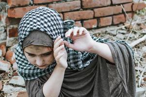 a refugee child in the war, a Muslim girl with a dirty face on the ruins, the concept of peace and war, the child is crying and waiting for help. photo