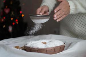 Las manos de una mujer espolvorean azúcar en polvo en un pastel de Navidad. año nuevo y navidad. de cerca. foto