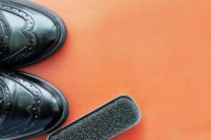 una esponja para zapatos junto a zapatos de cuero negro pulido sobre un fondo naranja con espacio para texto. foto