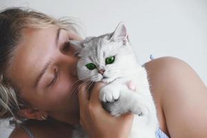 una hermosa joven besa a un gato blanco con ojos verdes. chinchilla de plata británica. foto