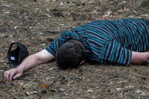 Murder in the woods. The body of a man in a blue t-shirt lies on the ground among the trees in the forest. Victim of an attack. photo