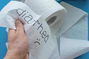 Toilet paper with the word diarrhea in the person's hand on the background of toilet paper rolls. Close up. photo