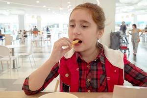 Adolescente hambrienta comiendo papas fritas en el patio de comidas del centro comercial. comida chatarra. foto