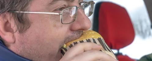 man wearing spectacles eats sandwich photo