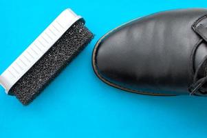 una esponja para zapatos junto a una bota de cuero negro pulido sobre un fondo azul.